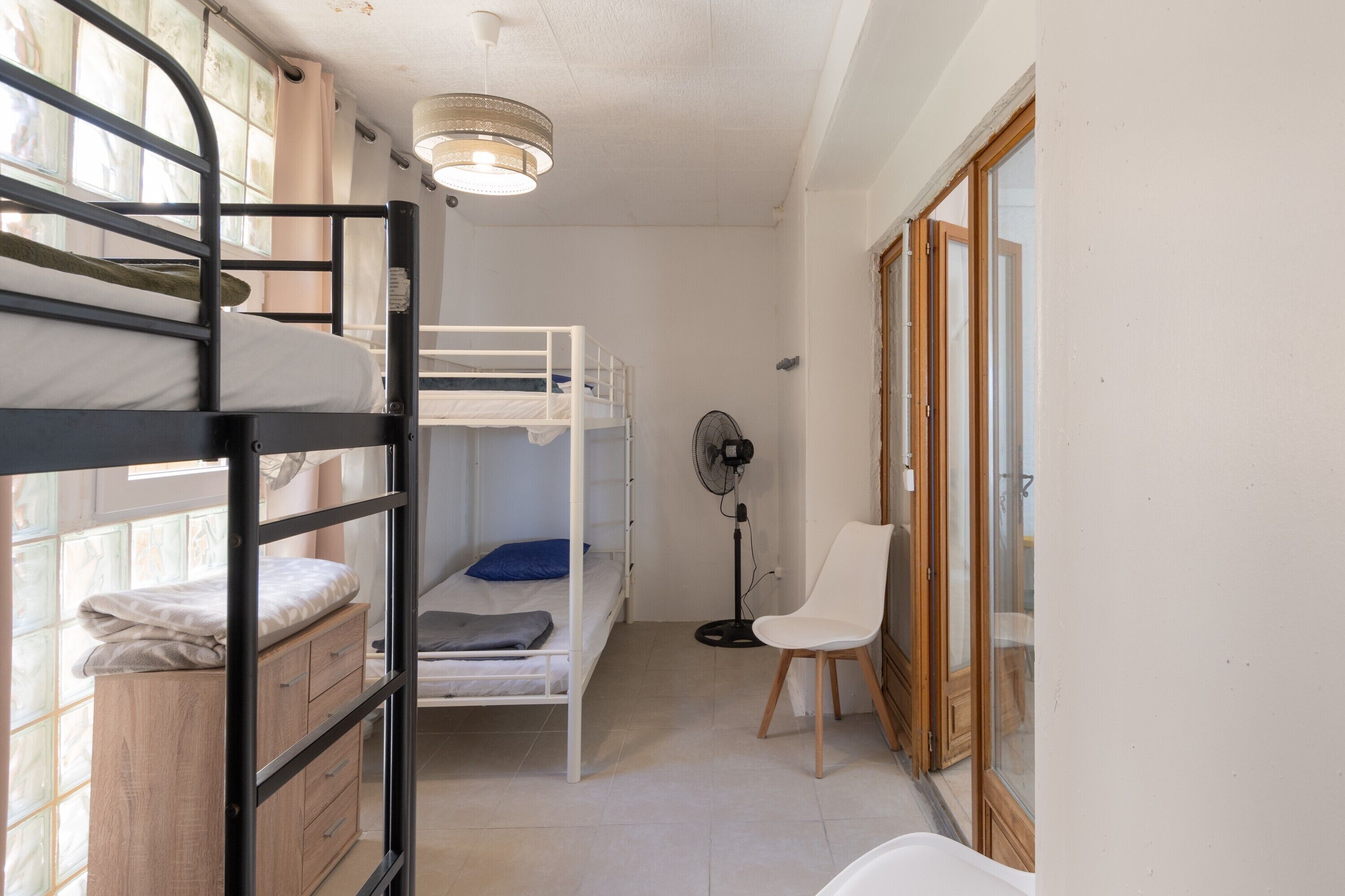 Ein Schlafsaalzimmer mit Etagenbetten, einem Ventilator, einem Stuhl und einem Fenster.