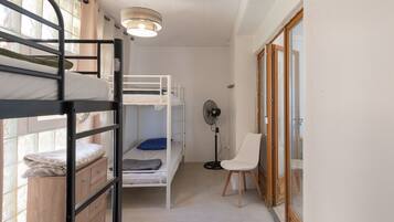Ein Schlafsaalzimmer mit Etagenbetten, einem Ventilator, einem Stuhl und einem Fenster.
