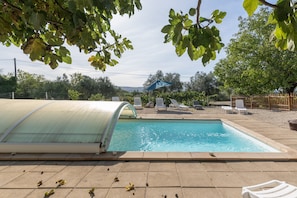 Une piscine dotée d’un espace couvert, de chaises longues et bordée d’arbres.