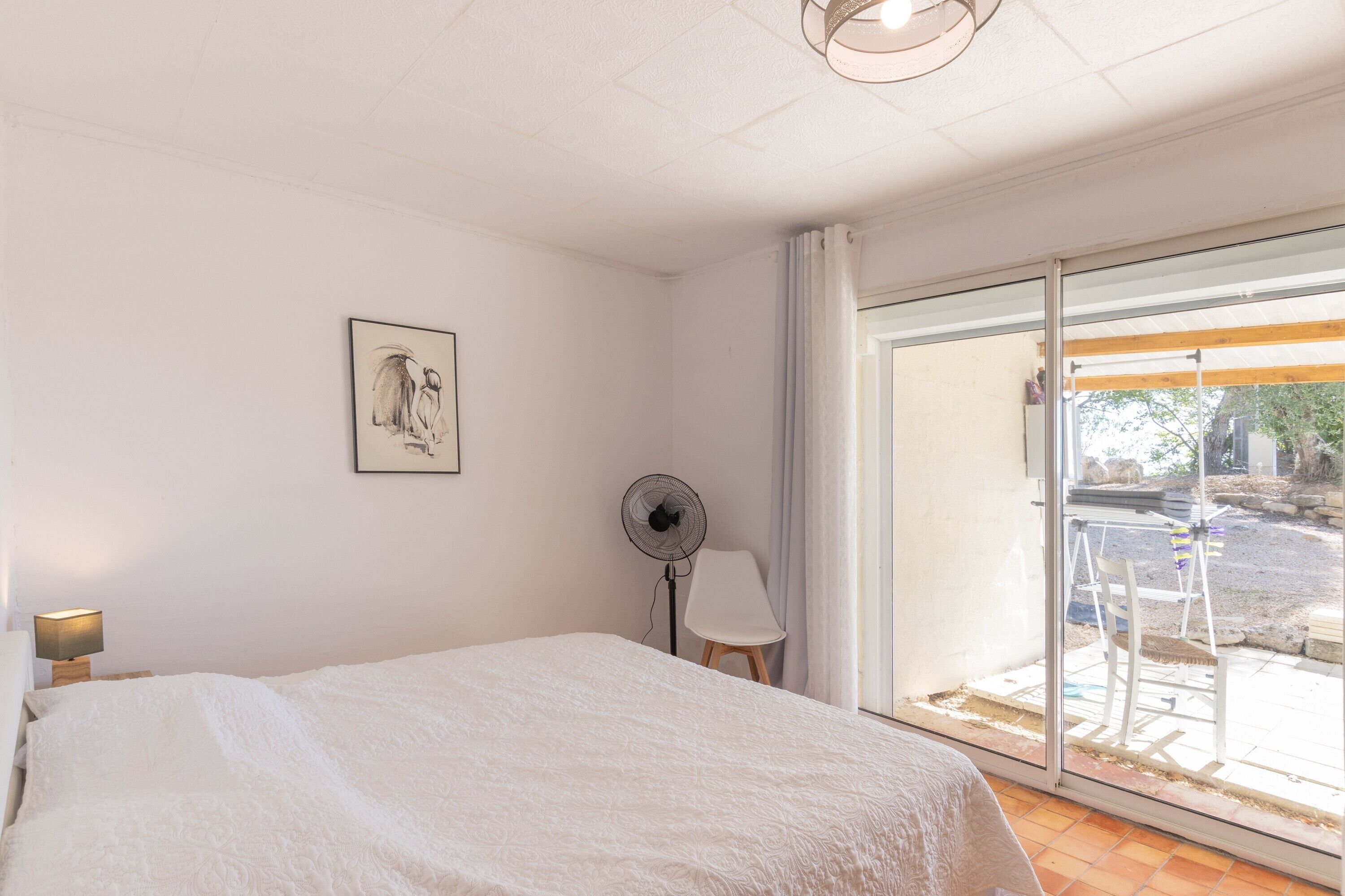 Et soveværelse med seng, ventilator, stol og et vindue med udsigt.