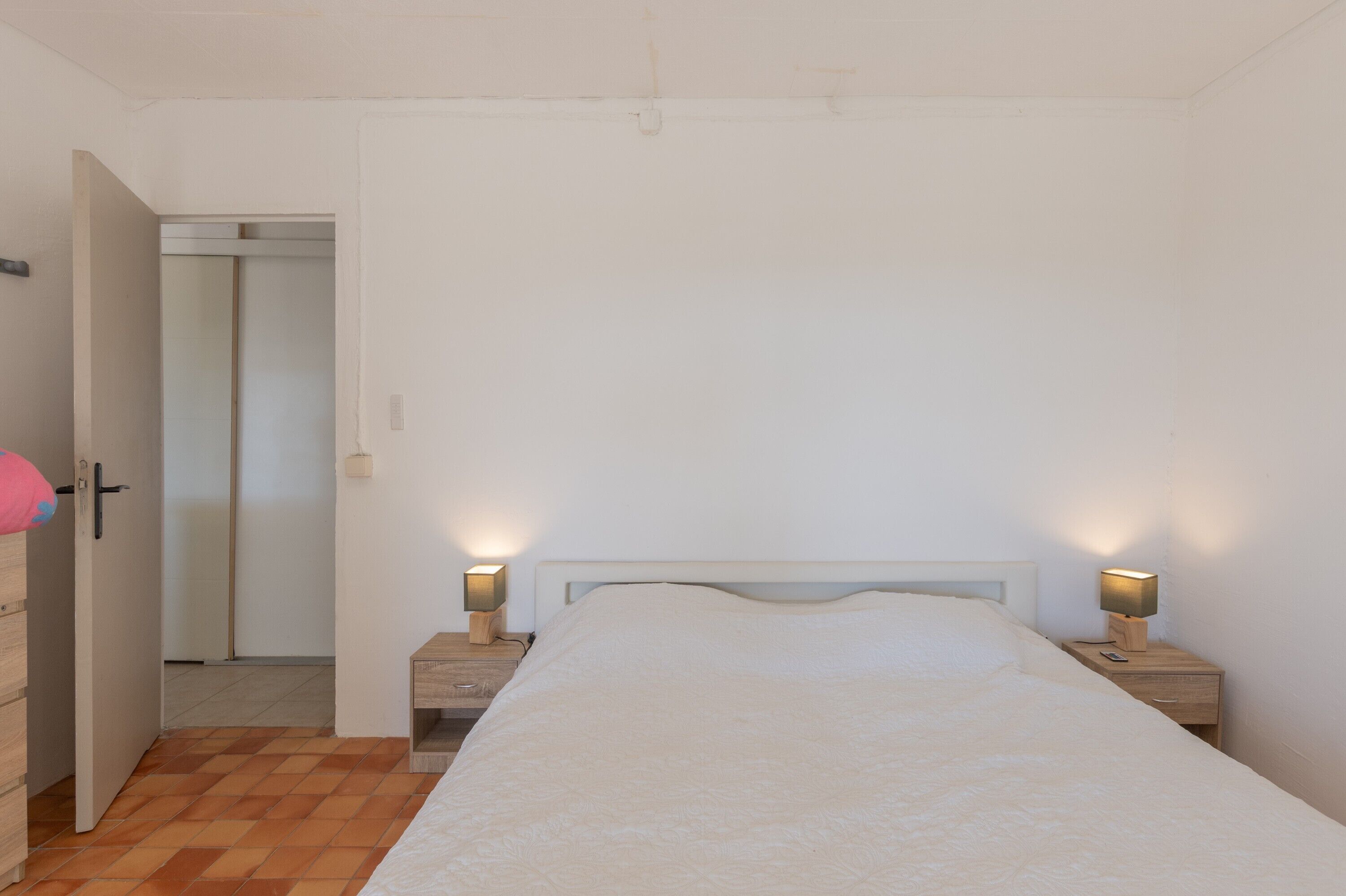 A bedroom with a bed, two bedside tables with lamps, a wooden door, and a white wall.