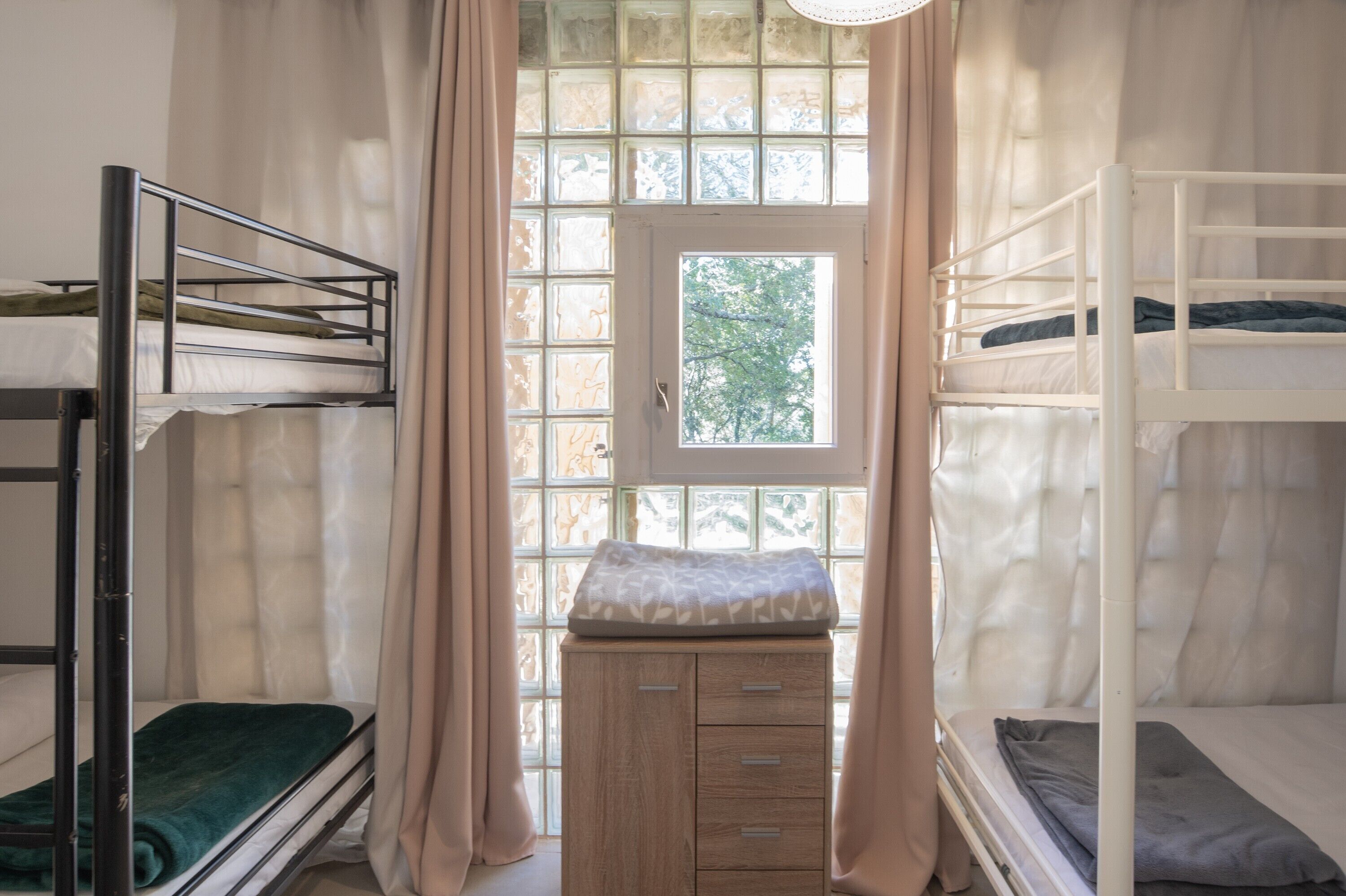Un dormitorio con literas, una ventana con cortinas y un pequeño armario de madera.