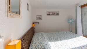 Ett sovrum med en säng, en spegel, en väggmonterad fläkt och en liten hylla med en lampa.
