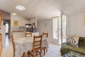 A kitchen with white cabinets, a dining table with chairs, a sofa, and a sliding glass door leading to an outdoor area.