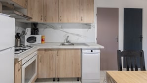 A compact kitchen with wooden cabinets, a white dishwasher, a gas stove, and a microwave. - Holiday Home 'Gîte 1 - La Tour' with Lake View and Wi-Fi (Saint-Sauveur de Cruzières)