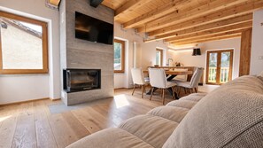 A modern living room with a fireplace, wooden floors, and a dining area with chairs and a table. - Alpine Chic Retreat (Courmayeur)