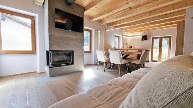 Un salon moderne doté d’une cheminée, d’un plafond en bois et d’un coin repas avec des chaises et une table.