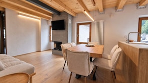 A modern living room with a wooden ceiling, a fireplace, a dining table with chairs, and a television mounted on the wall. - Alpine Chic Retreat (Courmayeur)