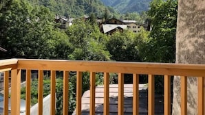 Un balcon doté d’une balustrade en bois, offrant une vue sur un paysage montagneux parsemé de maisons et de verdure.