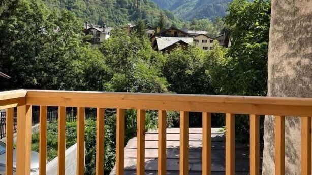 A balcony with a wooden railing overlooking a mountainous landscape with houses and greenery. - Alpine Chic Retreat (Courmayeur)