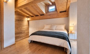 A bedroom with a wooden ceiling, a bed with white and dark bedding, and a small window. - Alpine Chic Retreat (Courmayeur)