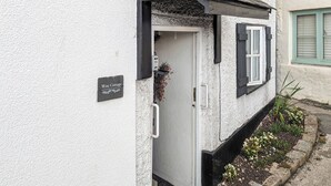 Une petite maison aux murs blancs, à la porte noire et sur laquelle on peut lire l’inscription « Wee Cottage ».