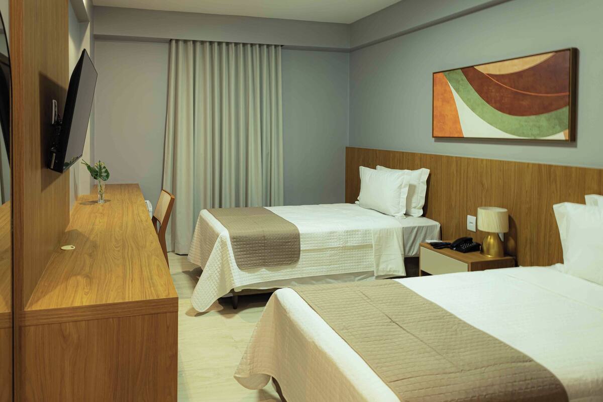 Ein Hotelzimmer mit zwei Betten, einem Schreibtisch, einem Fernseher und einem Gemälde an der Wand.