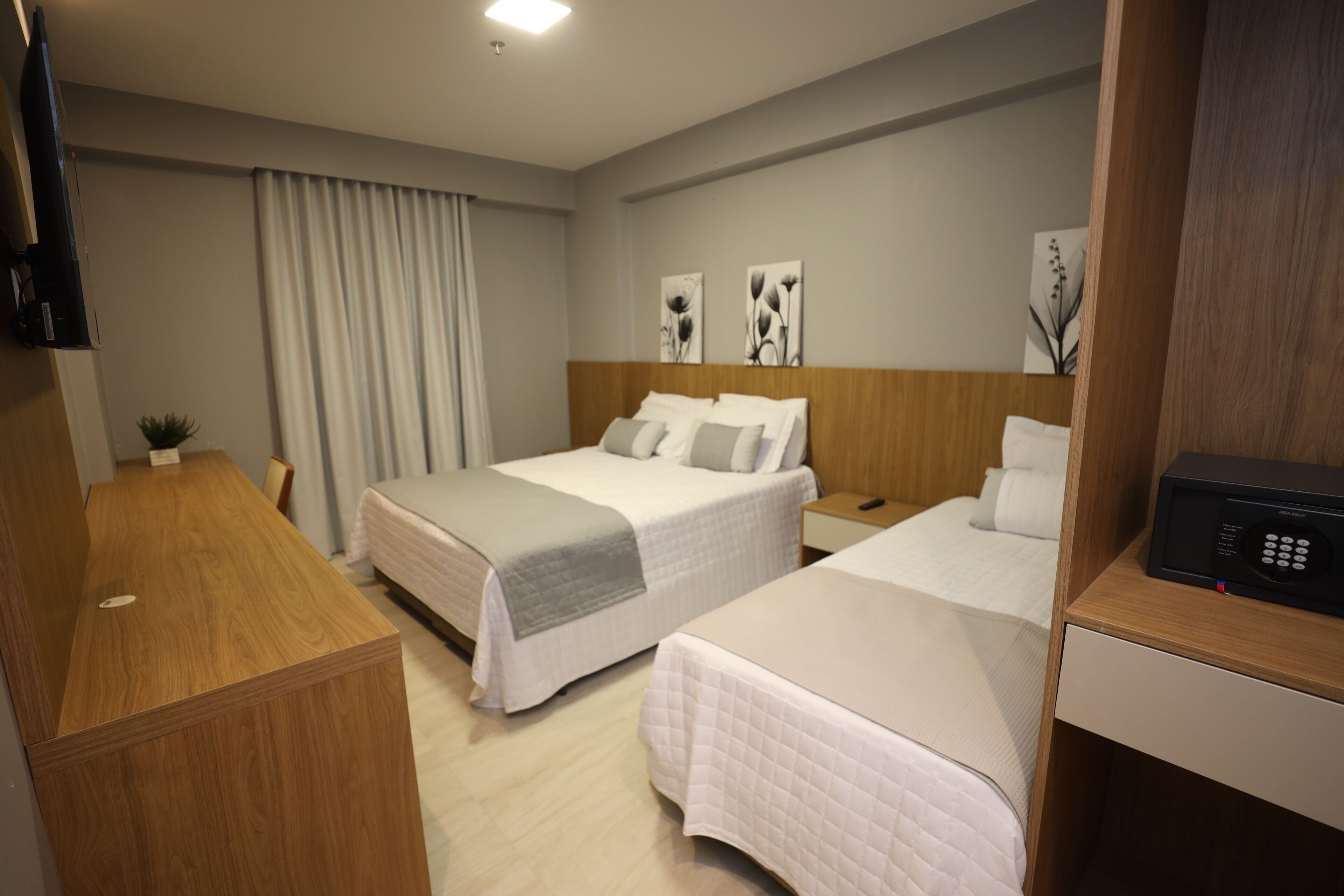 Quarto de hotel com duas camas, uma escrivaninha de madeira, televisão de tela plana e obras de arte na parede.