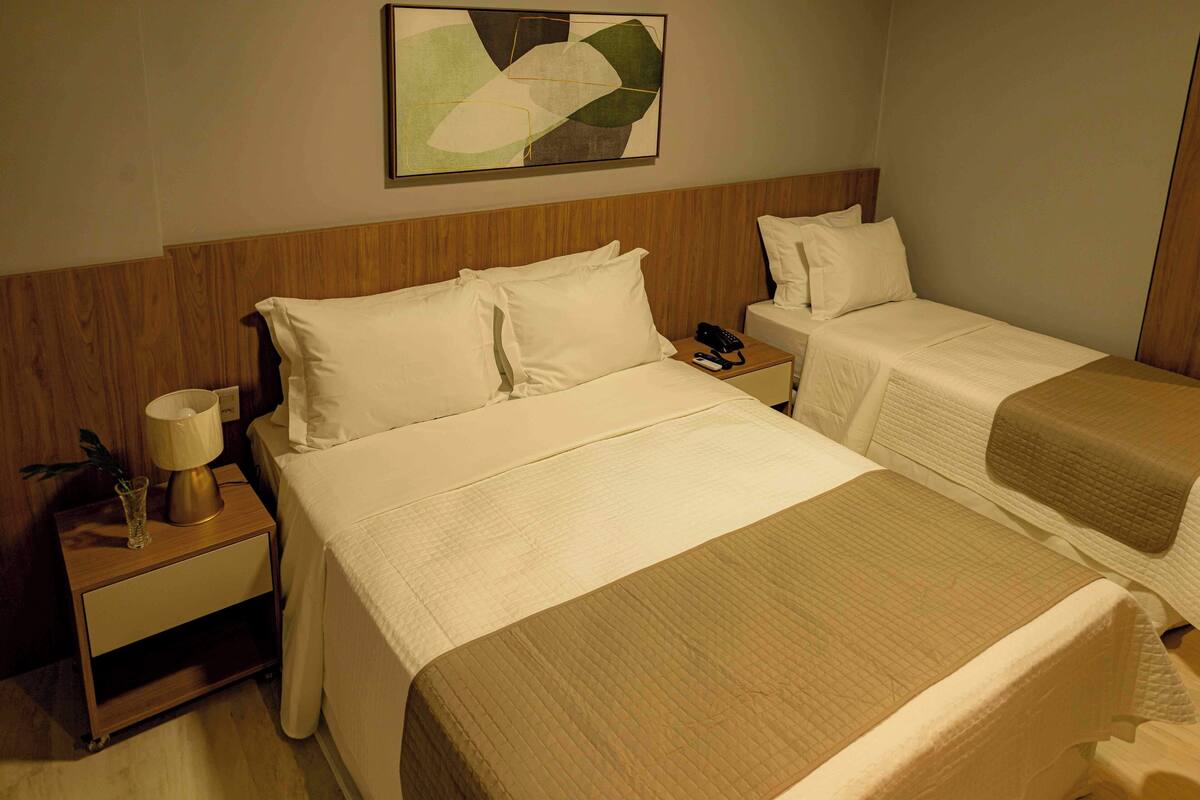 Ein Hotelzimmer mit zwei Betten, einem Nachttisch mit Lampe, einem Telefon und einem an der Wand hängenden, abstrakten Gemälde.