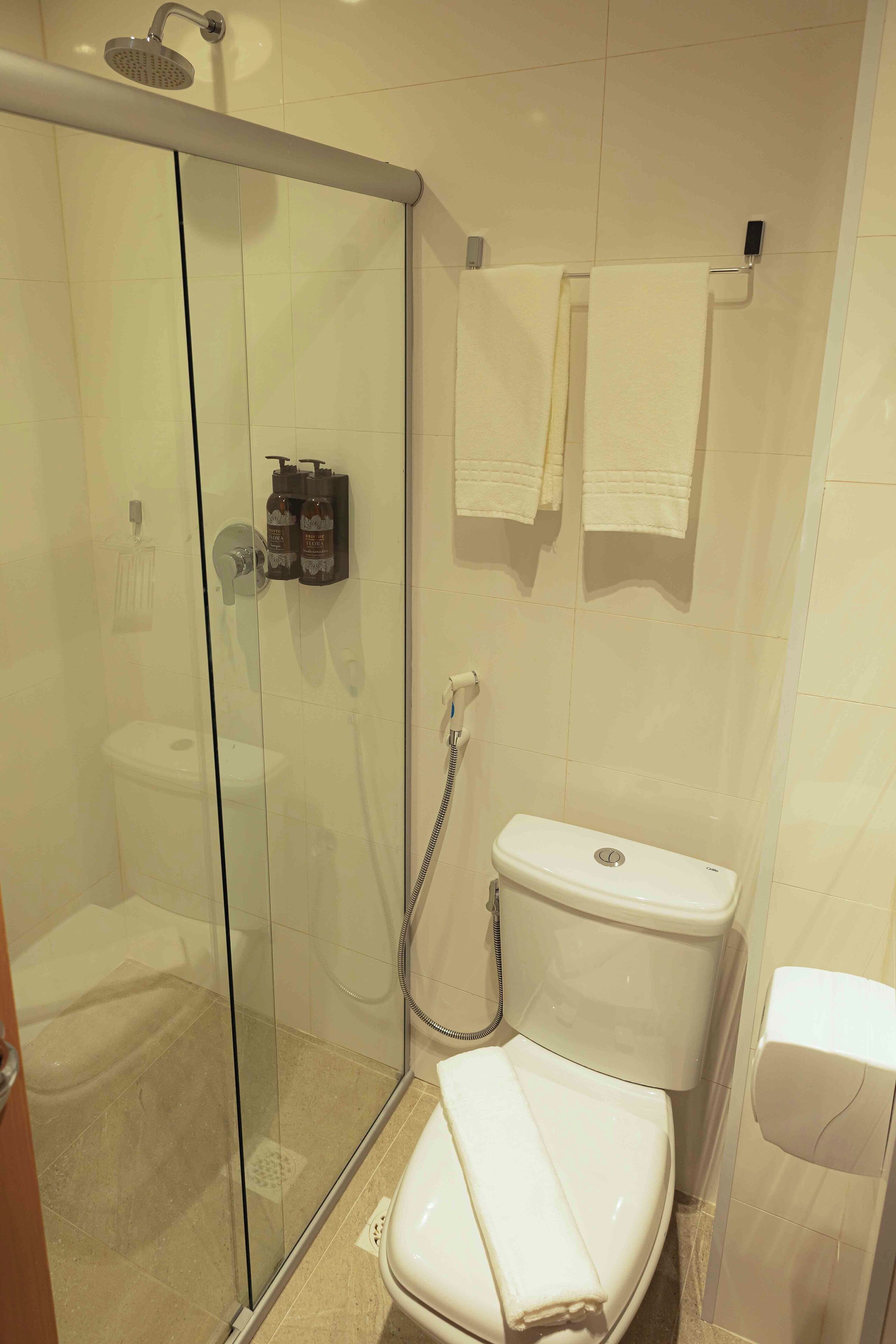 A bathroom with a glass-enclosed shower, a toilet, and a towel rack with towels.