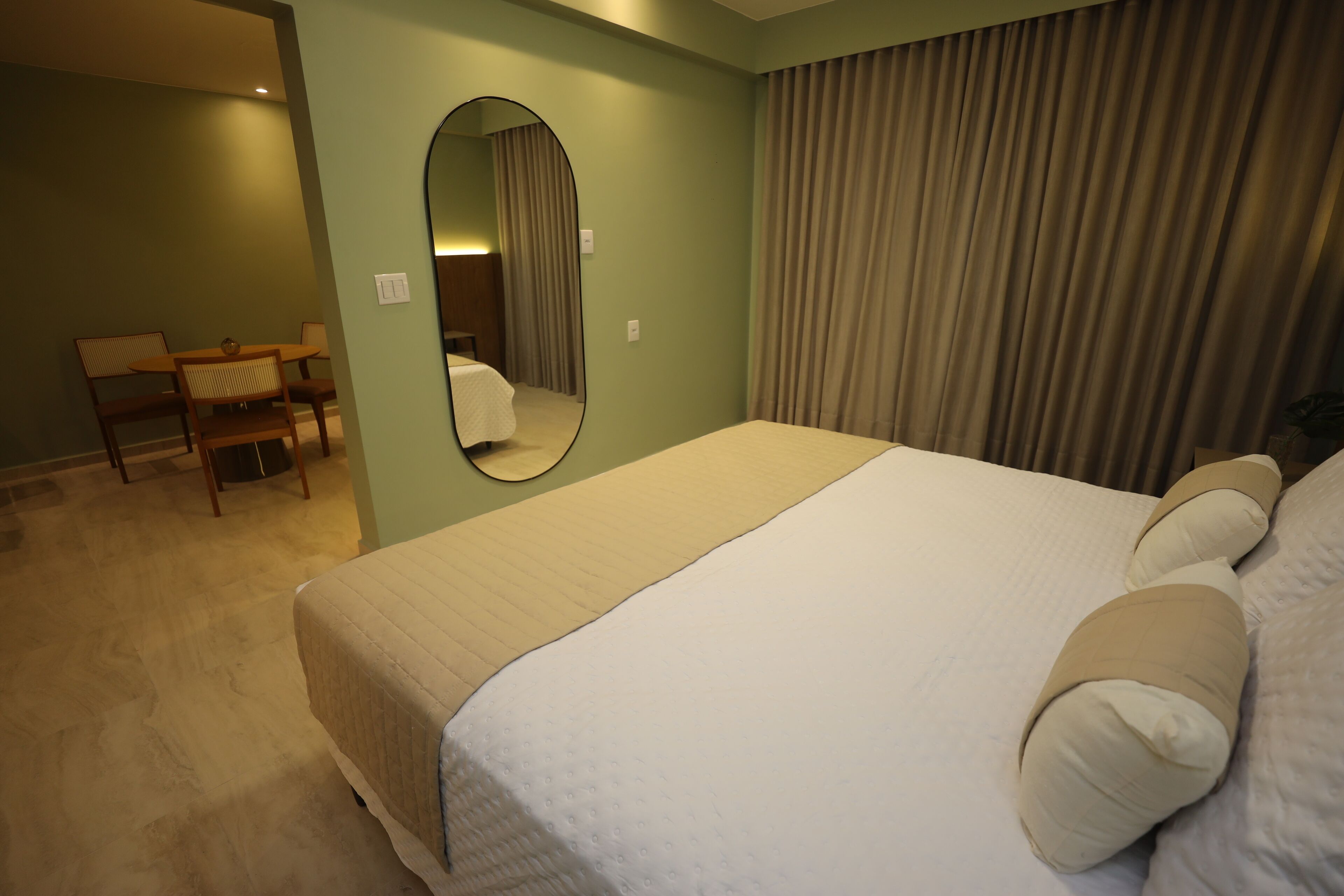 Habitación de hotel con una cama grande, una silla, una mesita y un espejo en la pared.