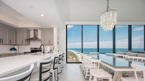 A modern kitchen with a large island, white cabinetry, and a view of the beach through large windows. - Phoenix Gulf Shores Ii 2205 4 Bedroom Condo (Gulf Shores)