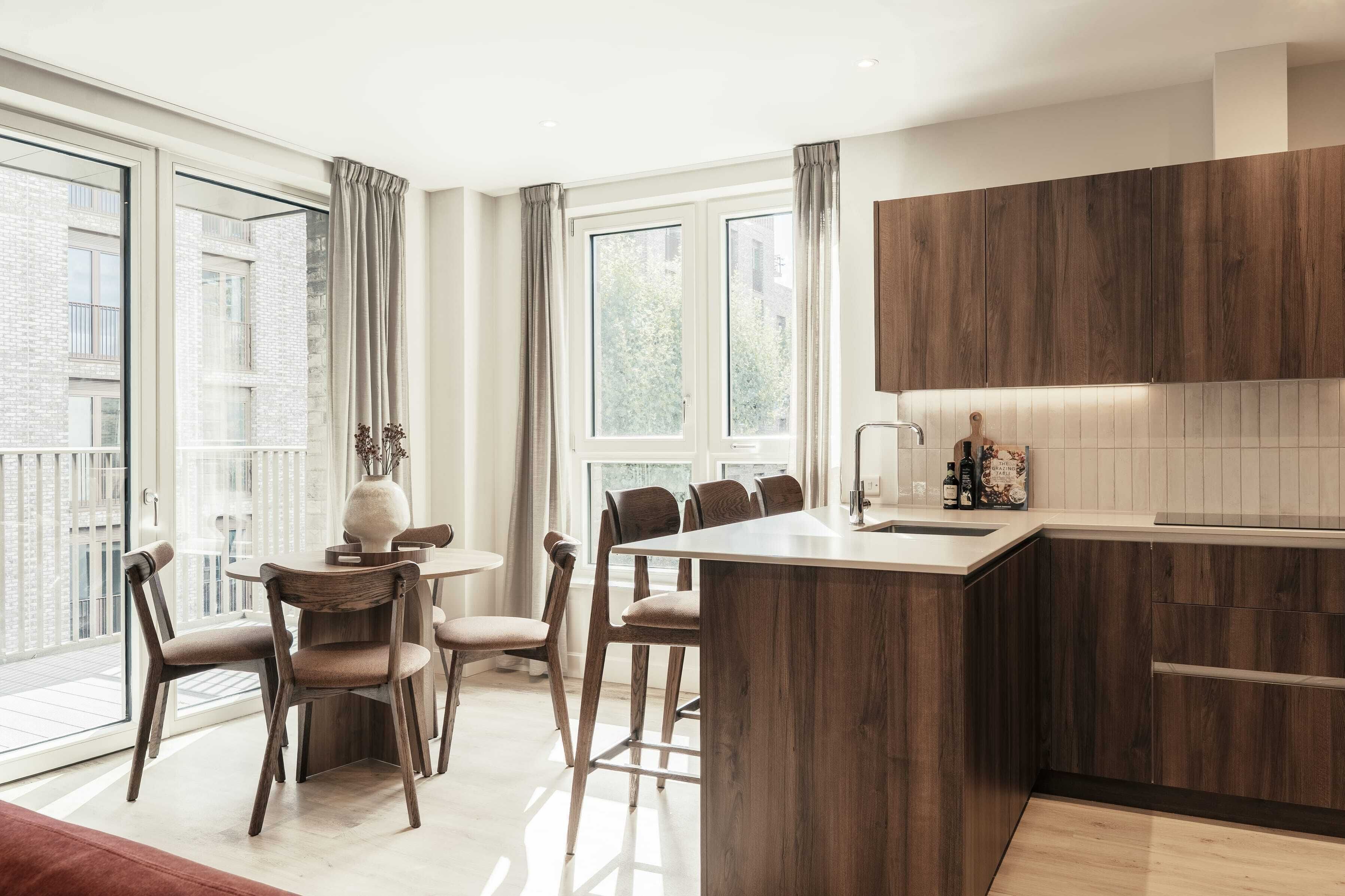 Una cocina moderna con una isla de madera, ventanas amplias y un comedor con sillas.
