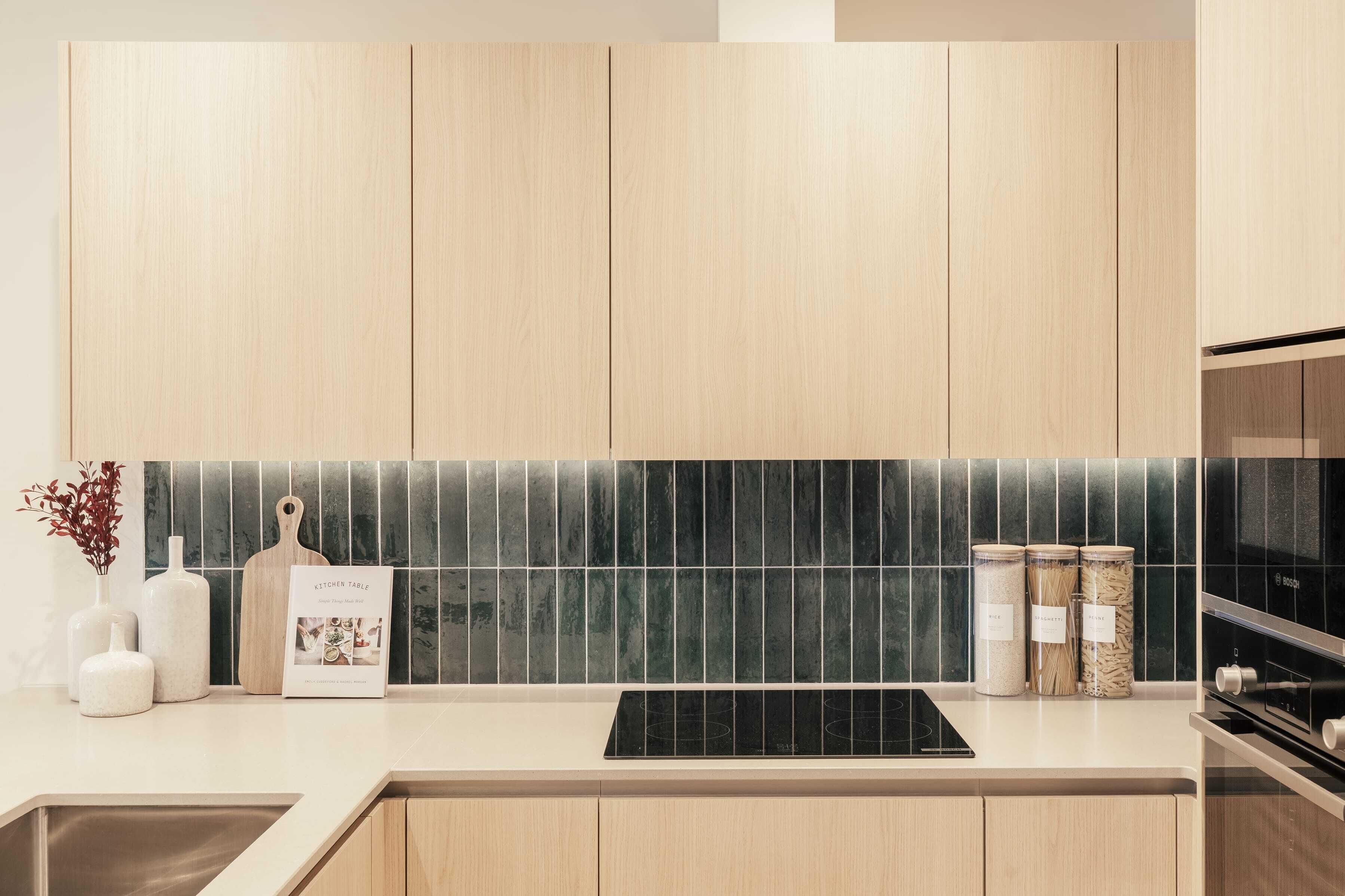 Una cocina moderna con armarios de madera, una placa de inducción negra y un salpicadero de azulejos.