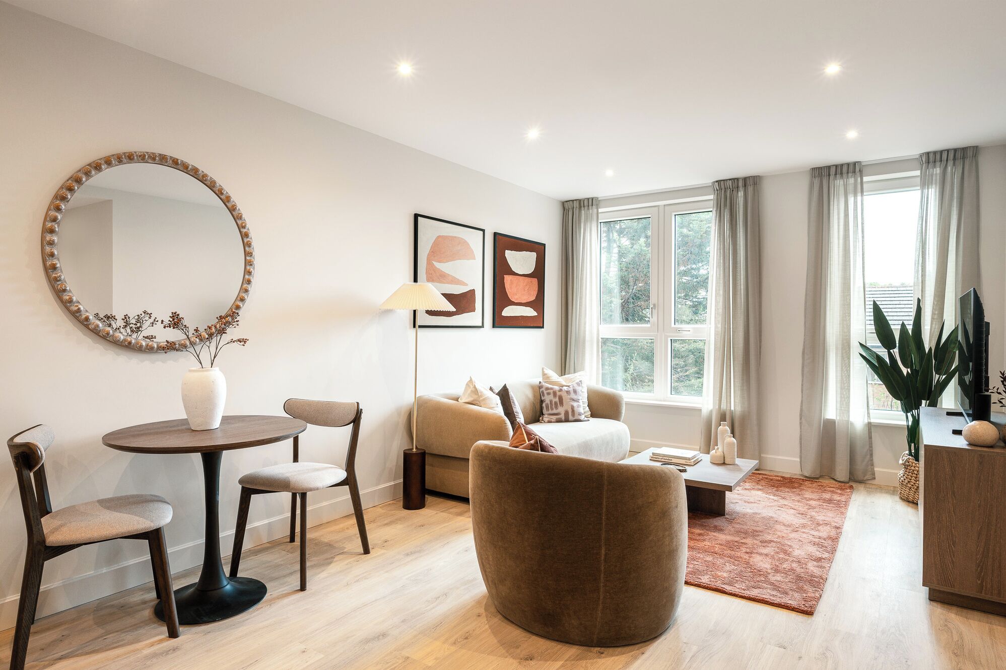 Ein modernes Wohnzimmer mit einem runden Spiegel, einem runden Tisch, einer Couch und einem Couchtisch. Zwei Sessel, eine Lampe und Kunstwerke zieren die Wand.