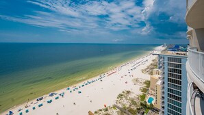 A beach view from a high-rise hotel with a clear sky, a sandy beach, and a pool.