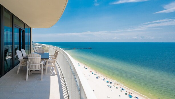 A balcony with a table and chairs overlooking a beach with a pier in the distance.