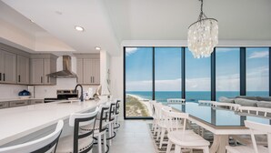 A modern kitchen with a large island, white cabinetry, and a view of the beach through large windows.