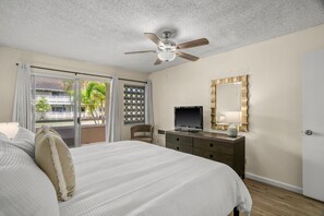 Quarto de hotel com cama, televisão, penteadeira, espelho e ventilador de teto.
