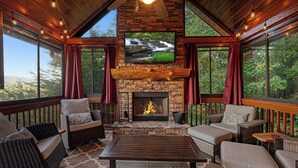 A cozy outdoor seating area with wicker furniture, a fireplace, and large windows offering a view of the outdoors. - God's View - Pet Friendly, Blue Ridge GA (Blue Ridge)