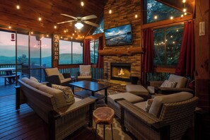 A cozy outdoor seating area with wicker furniture, a fireplace, and a TV mounted on the wall. - God's View - Pet Friendly, Blue Ridge GA (Blue Ridge)