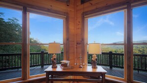 A wooden deck with large windows, a table with two lamps, and a book. - God's View - Pet Friendly, Blue Ridge GA (Blue Ridge)