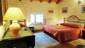 A bedroom with a bed, a nightstand, a lamp, a window, and a radiator.
