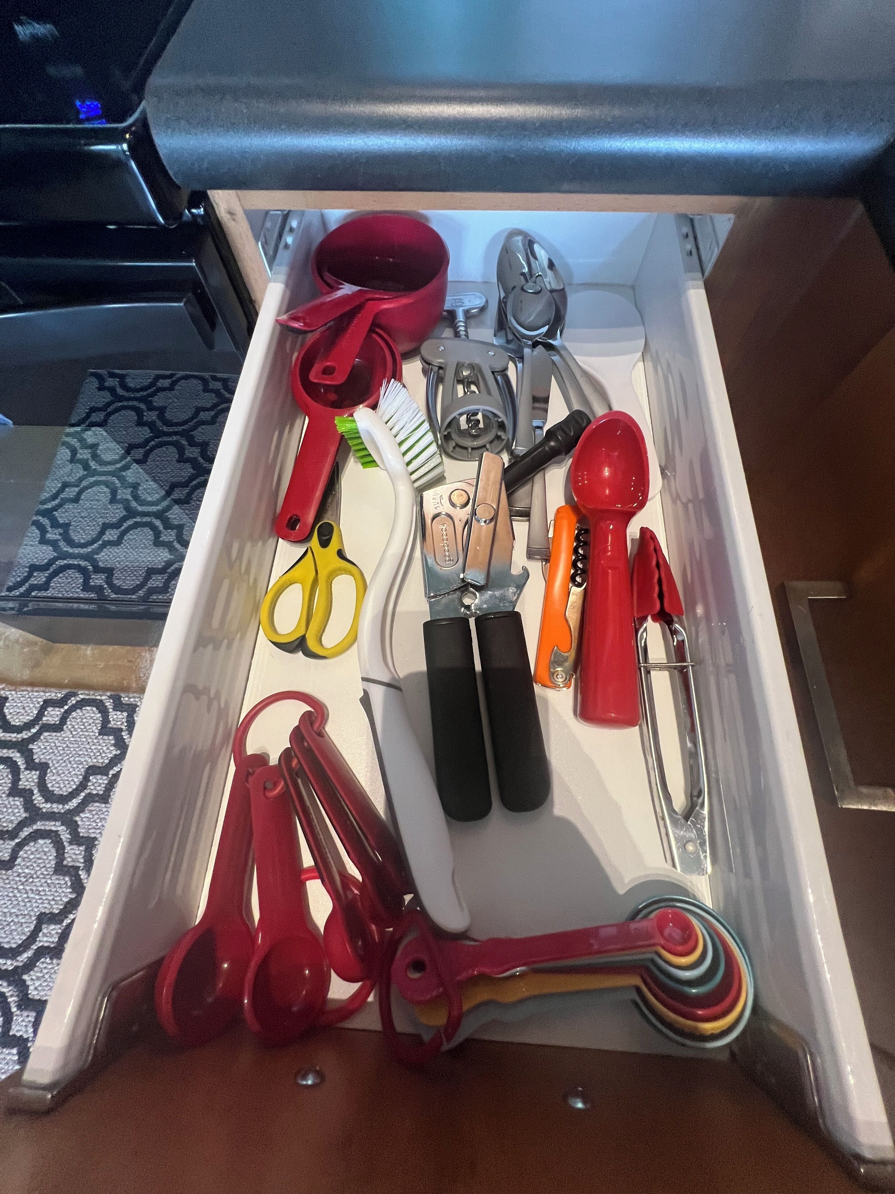 A drawer with various tools and utensils, including scissors, a hammer, and a screwdriver.