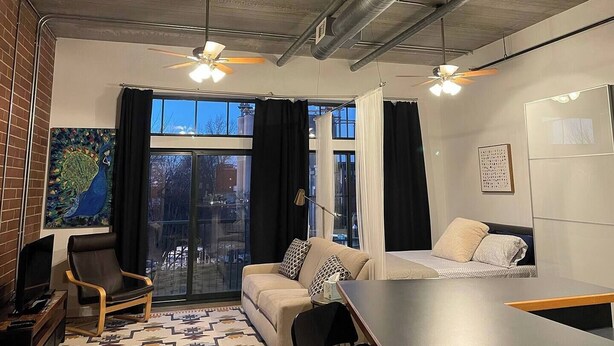 Un salon moderne avec un canapé, une table à manger et un téléviseur. Il y a deux ventilateurs de plafond et une grande fenêtre avec des rideaux.