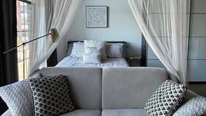 Une chambre à coucher moderne avec un lit, un canapé gris et des rideaux légers.
