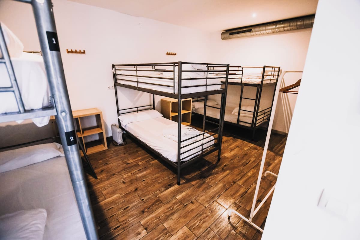 Une chambre de dortoir avec des lits superposés, un plancher en bois et une petite table de chevet.