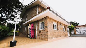 Una casa de dos pisos con fachada de ladrillo, un patio con baldosas y una tabla de surf roja apoyada contra la pared.