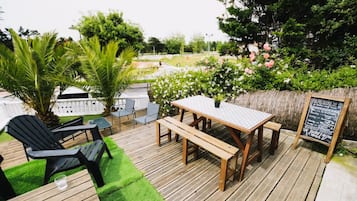 Una terraza exterior con mesa y sillas de madera, un pequeño jardín con una palmera y un cartel de pizarra.