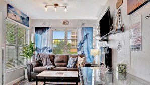 A living room with a brown leather sofa, a glass coffee table, and a TV mounted on the wall. - Seashell Suite 1B Pet Friendly Waterfront Dock (Treasure Island)