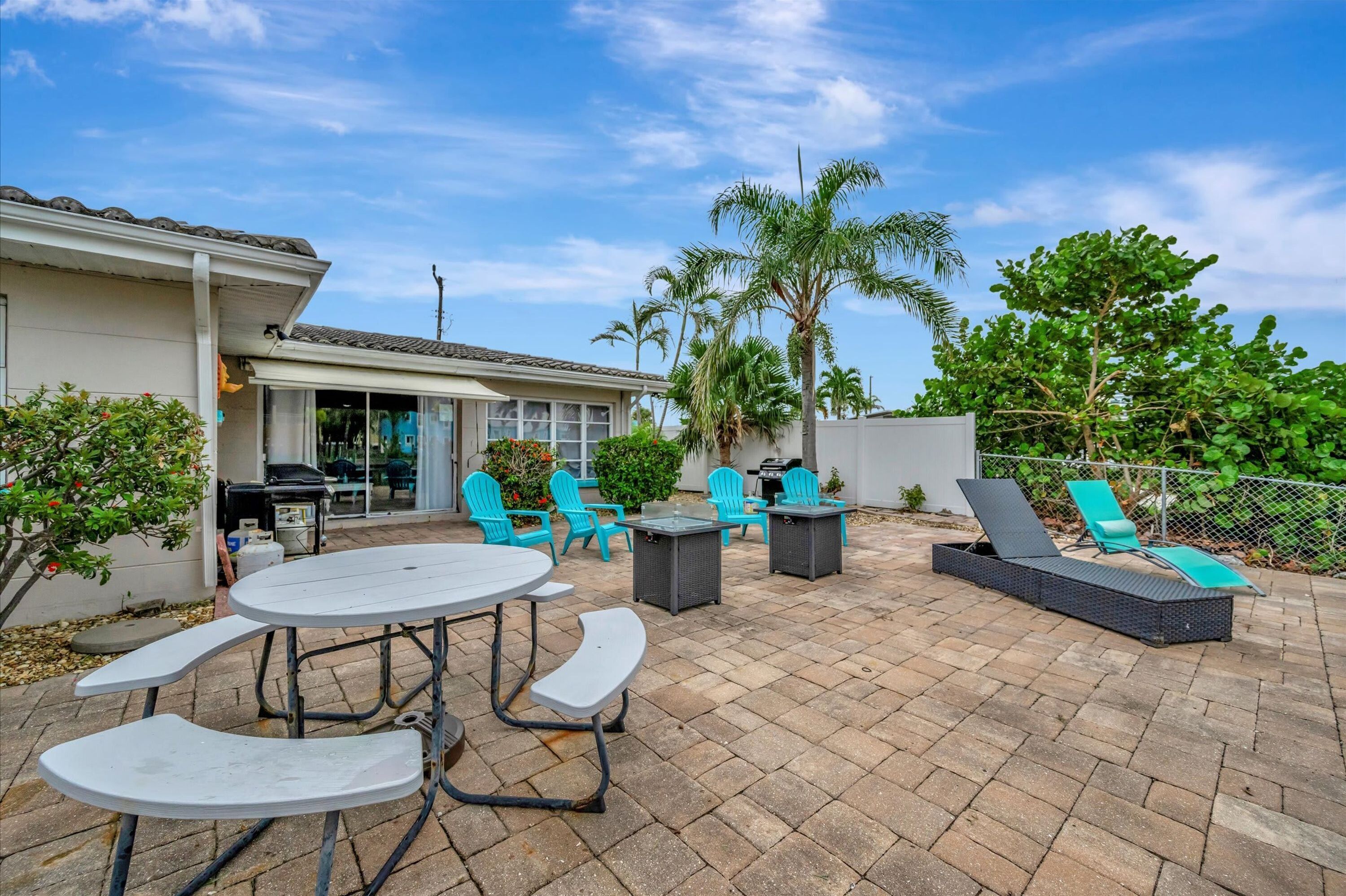An outdoor patio area with a round table, blue chairs, and a sun lounger.
