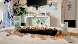 A room with a television mounted on the wall, a decorative shelf with various items, a small altar with candles and seashells, and a doormat with a seahorse and skull design. - Dolphin Suite 2B Pet Friendly Waterfront Dock (Treasure Island)