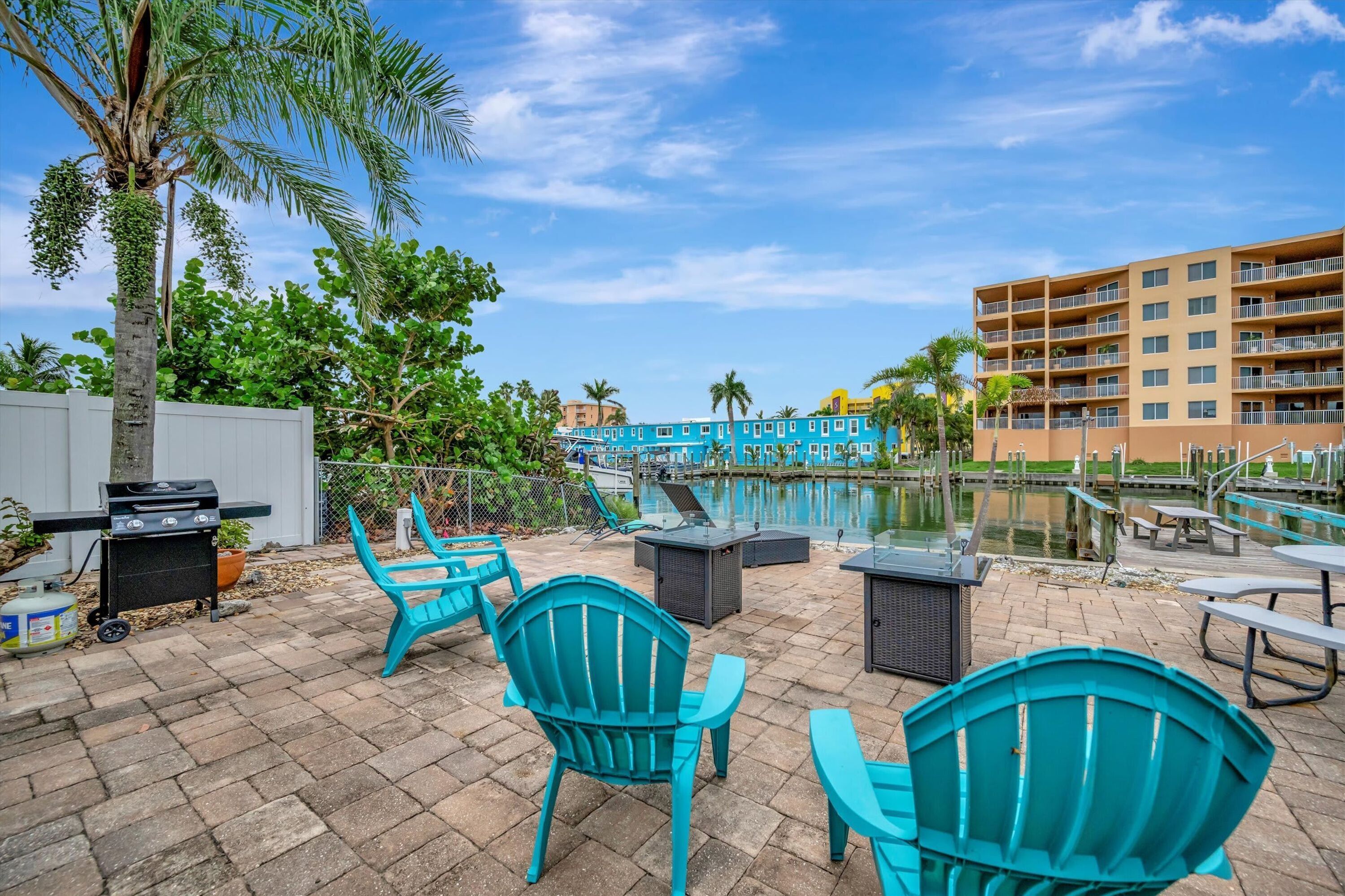 A patio area with turquoise chairs, a grill, and a pool.