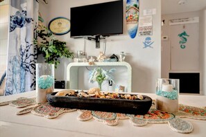 A room with a television mounted on the wall, a decorative shelf with various items, a small altar with candles and seashells, and a doormat with a seahorse and skull design. - Dolphin Suite 2B Pet Friendly Waterfront Dock (Treasure Island)