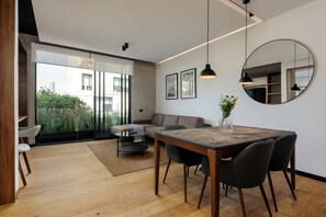 A modern living room with a wooden dining table, black chairs, a sofa, and a large window with a view of greenery. - w Fabulous 1BR With Elegant Balcony in Roma Nte (Mexico City)