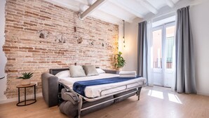 A modern bedroom with a brick wall, a bed, a small side table, and a potted plant.