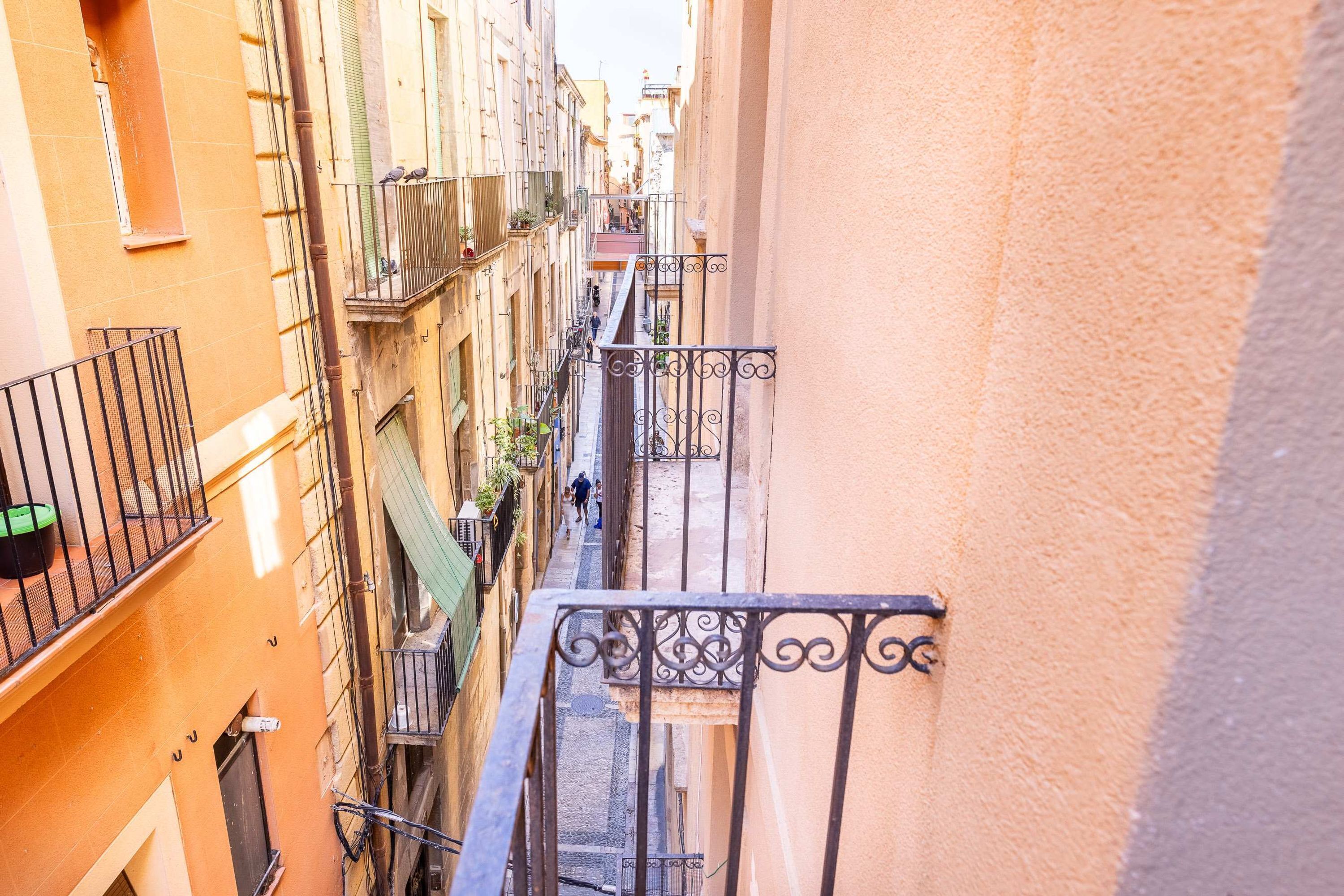 A narrow street between buildings with balconies, a bicycle, and a person walking.