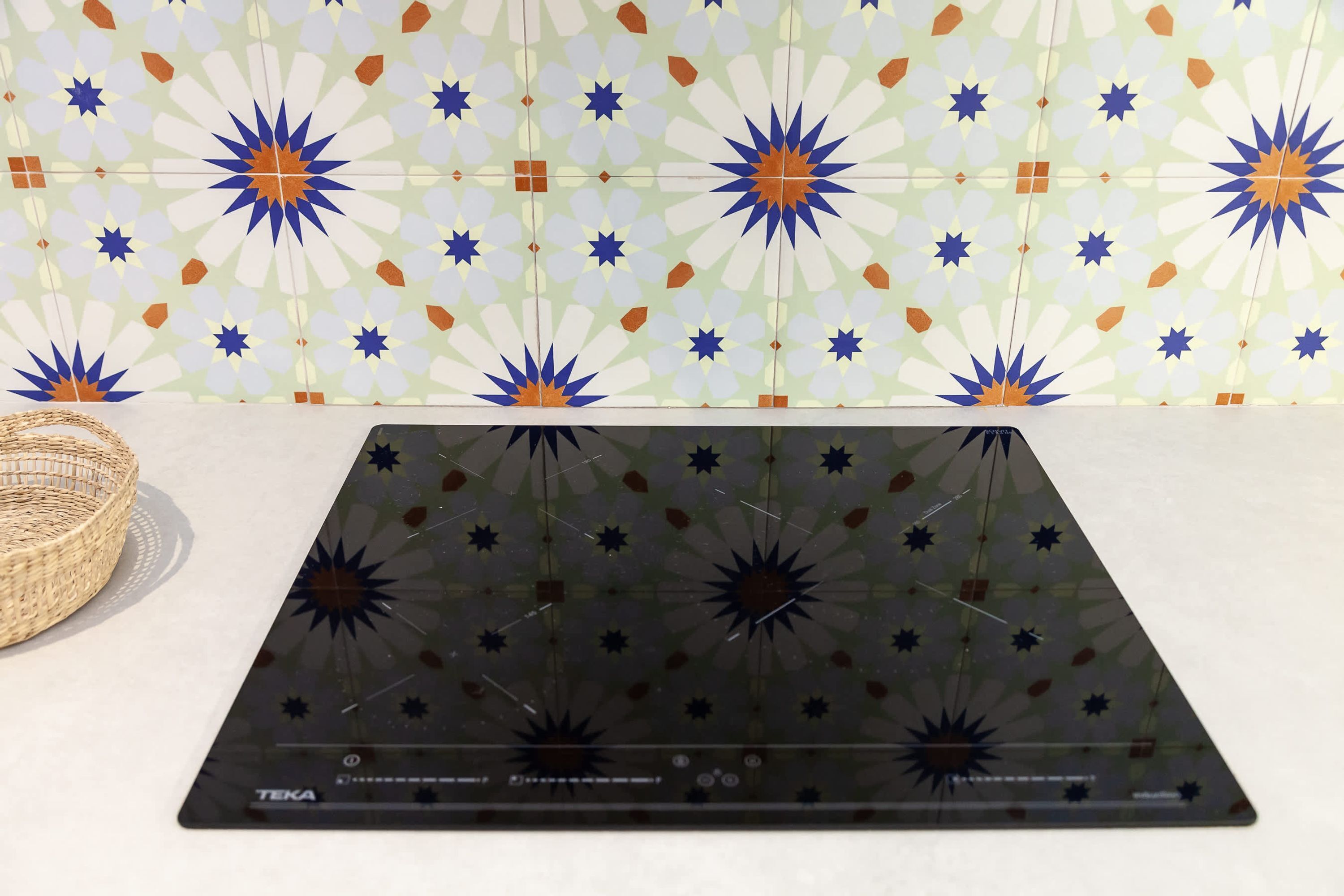 Una cocina con encimera negra, una cesta tejida y un salpicadero de azulejos con motivos florales.