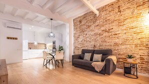 A modern living room with a brick wall, a grey sofa, and a dining area with a white table and chairs.