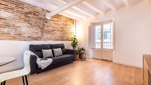 A cozy living room with a brick wall, a dark grey sofa, a white chair, and a wooden floor.